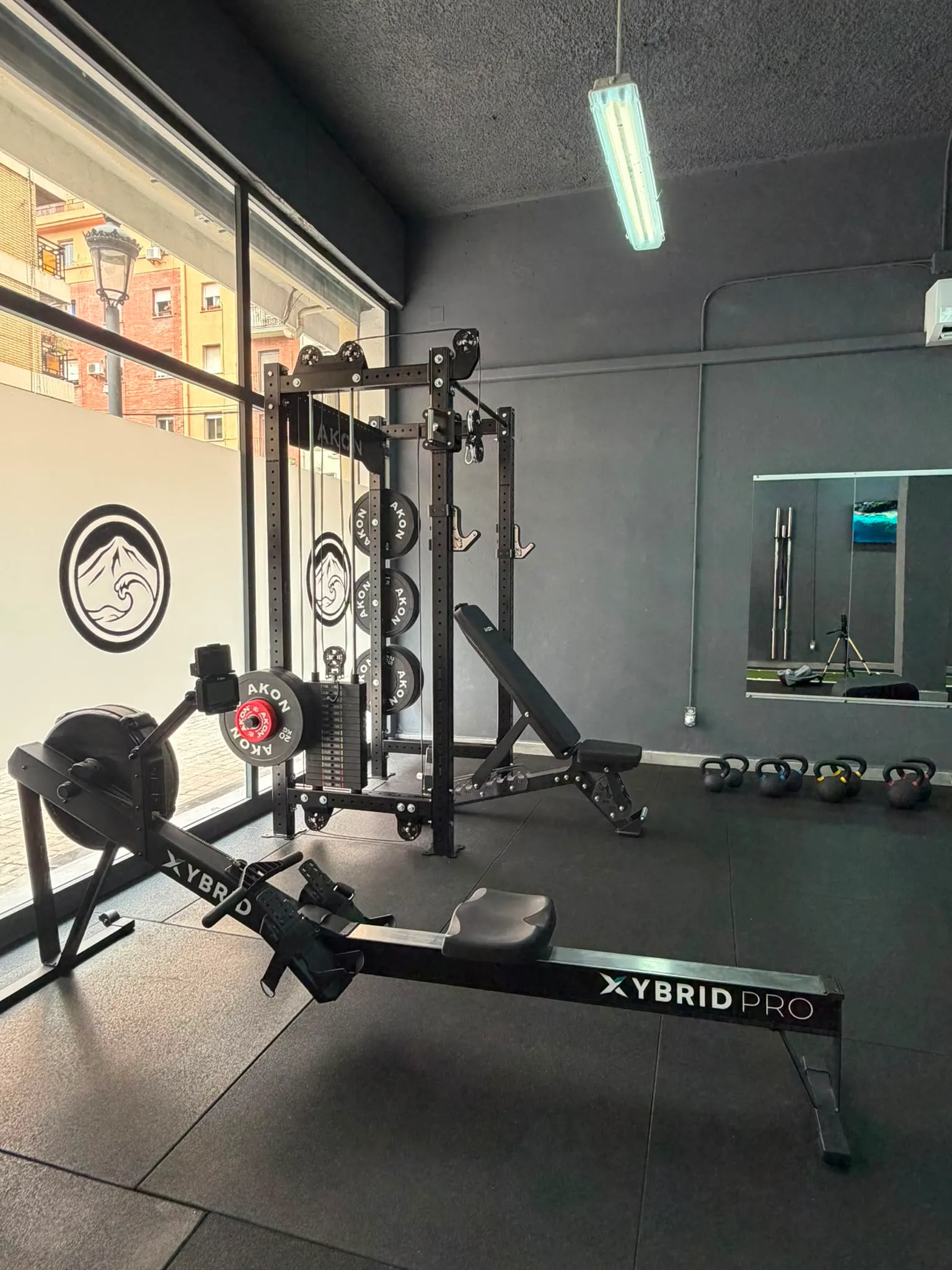 Sala de entrenamiento de Mencey Studio en Patraix, Valencia, con rack de fuerza, banco, remo y kettlebells junto al ventanal